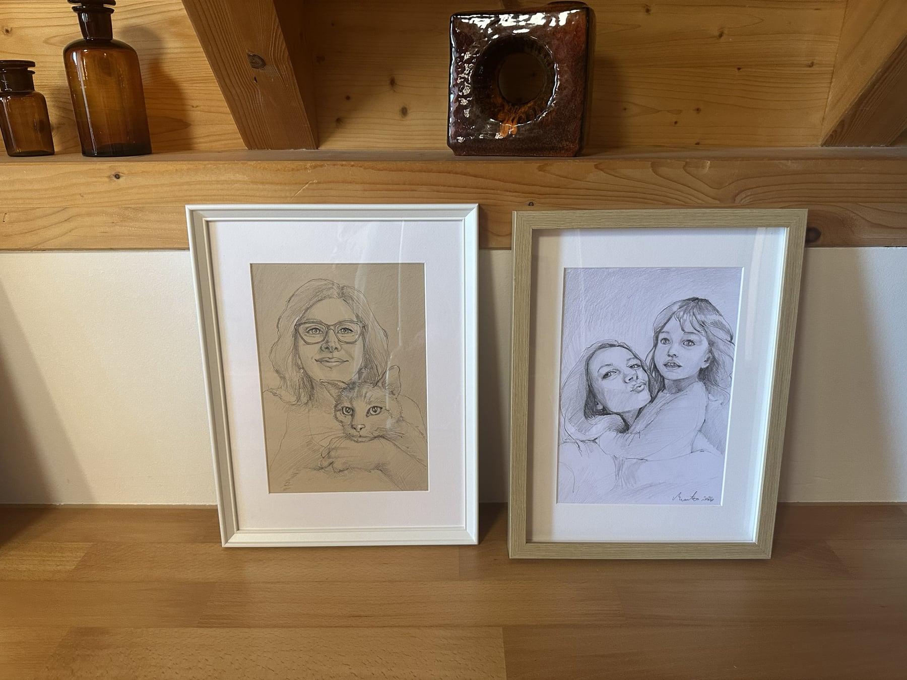 Zwei fertig gerahmte Bleistiftportraits auf einer Holzablage im Atelier.