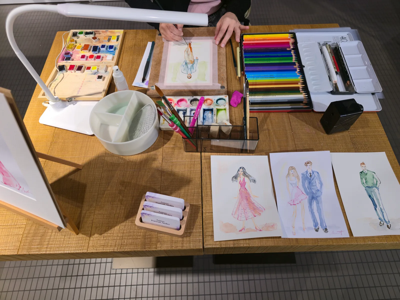 Vue de table avec matériel d'aquarelle et illustrations libres de mode et de personnes en pied présentées comme exemples de style.